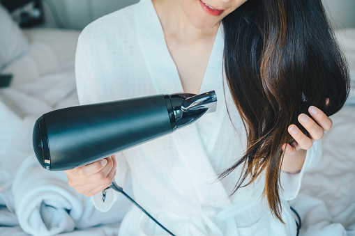 Mulher branca segurando o cabelo com a mão direita e com a esquerda usando um secador