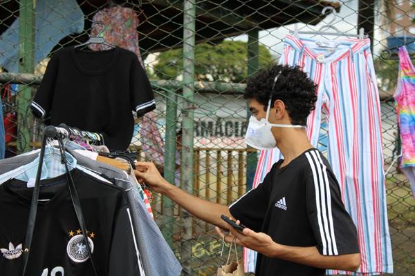 pessoa com máscara ao lado de arara de roupas