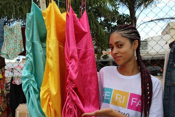 Mulher ao lado de arara com roupas coloridas