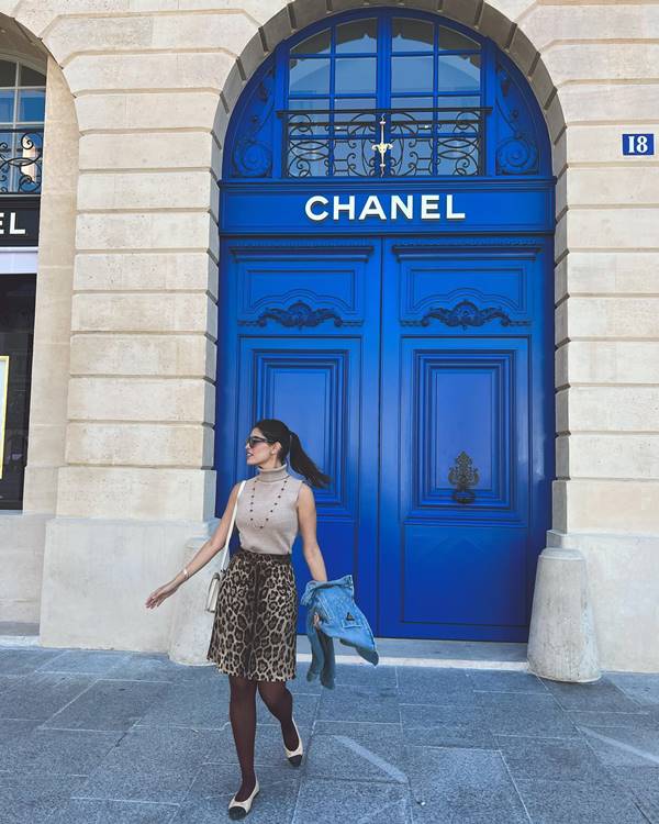 Mulher com look composto por saia e blusa na frente da loja da chanel