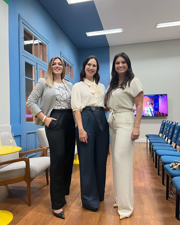 A consultora da moda Rachel Jordan, uma mulher branca, de meia idade e cabelo castanho médio, posando ao lado de duas mulheres