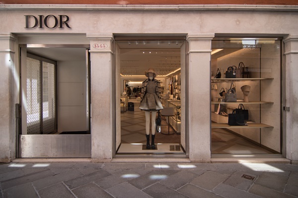 Fachada de loja da marca francesa Dior. O estabelecimento fotografado é na Itália e possui colunas de mármore, vitrine de vidro com manequim vestindo roupas da etiqueta.