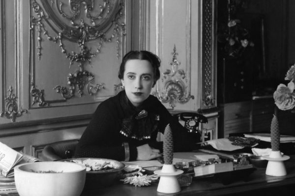 Retrato em preto e branco da estilista italiana Elsa Schiaparelli, em 1937, sentada à mesa - Metrópoles