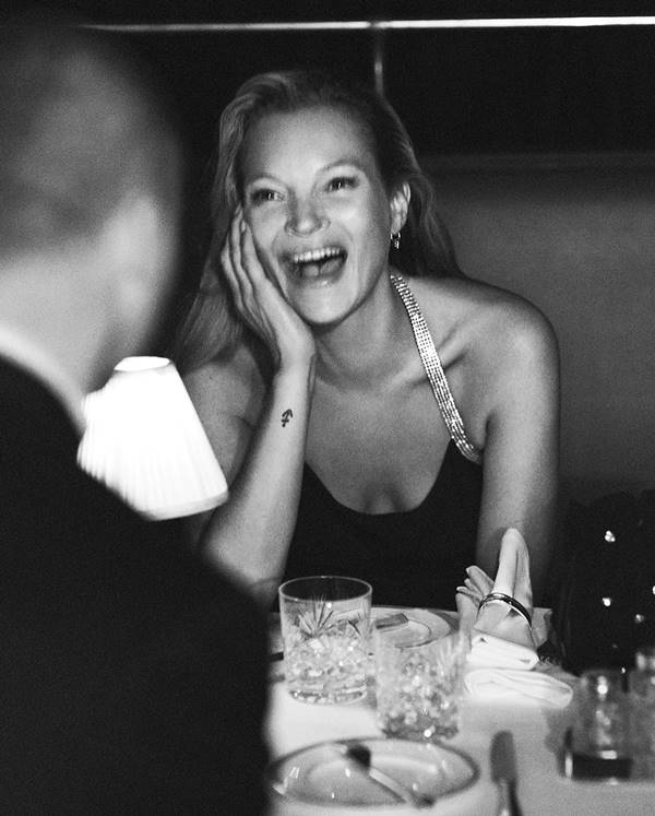 Kate Moss em mesa de restaurante, rindo em um retrato preto e branco 