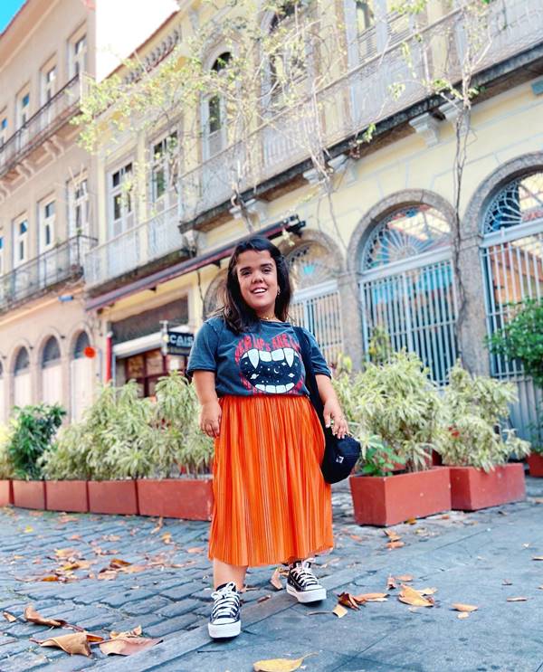 Mulher com nanismo usando saia laranja e camiseta com estampas