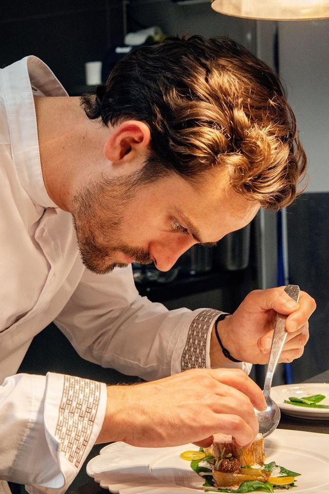 Foto colorida. Homem branco arrumar comida em um prato