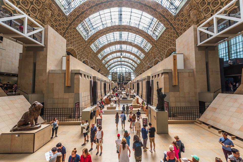 Foto colorida. Pessoas transitam no hall de um grande edifício