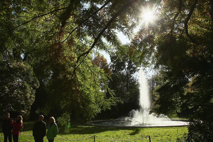 Foto colorida. Pessoas em um jardim com uma fonte