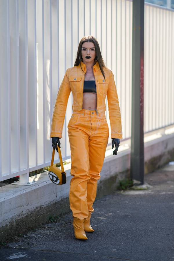 Julia Fox usando look amarelo com preto. Ela segura uma bolsa com logo da Diesel