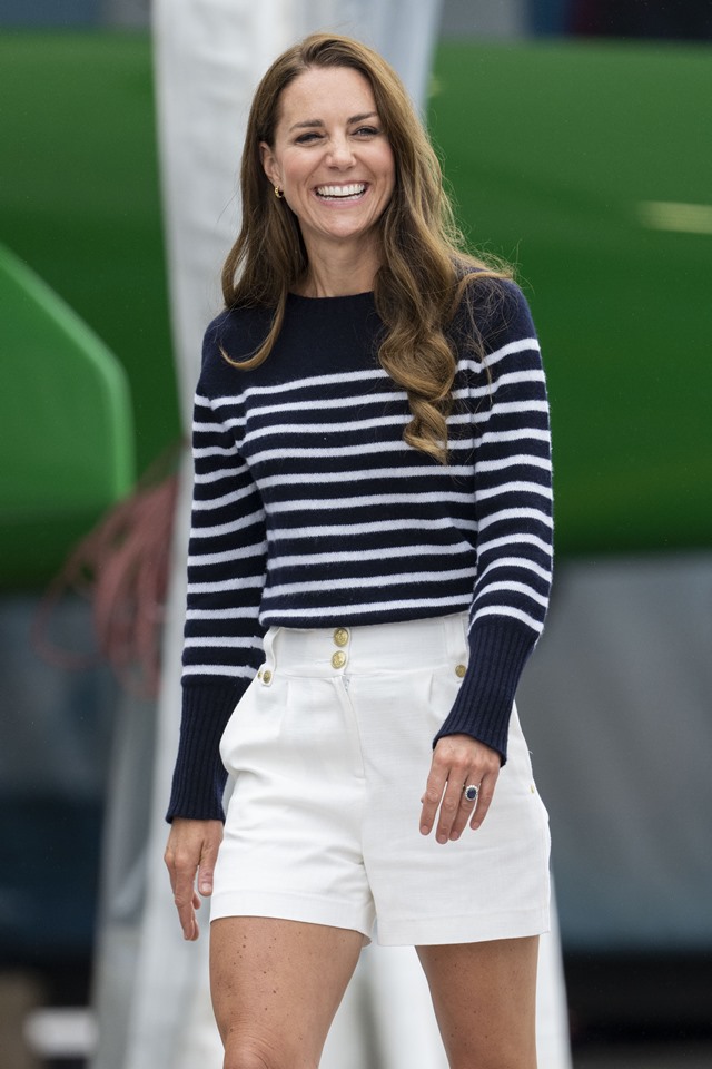 Foto colorida. Mulher sorridente com blusa listrada e shorts brancos