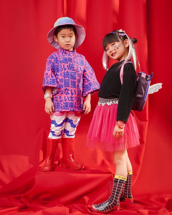 Duas crianças asiáticas posando para foto em um fundo vermelho. A imagem é da campanha publicitária da marca Sato Kid