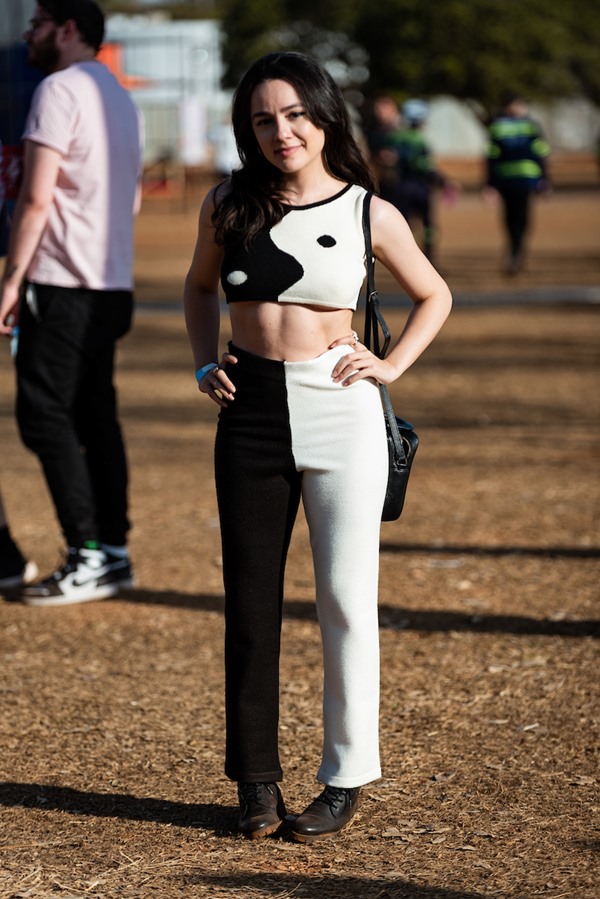 Mulher branca e jovem, de cabelo liso preto, posando para foto no Festival CoMA, em Brasília. Ela usa um top curto e uma calça, ambos metade preto e metade branco, formando o simbolo yin yang.