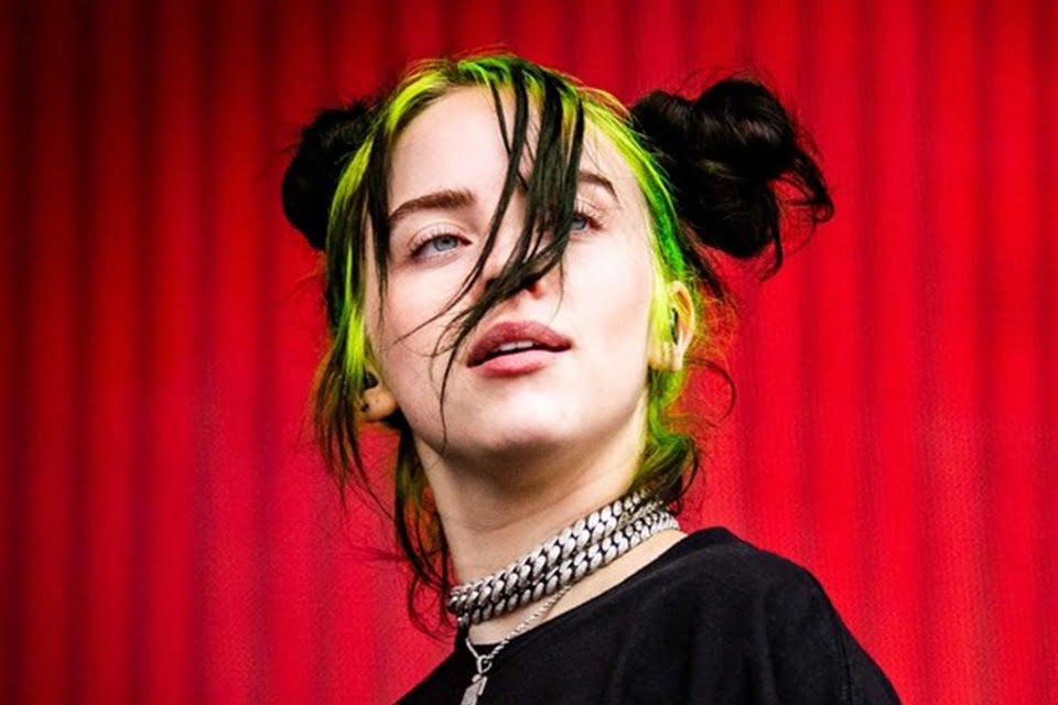 Foto colorida de Billie Eilish com um fundo vermelho - Metrópoles