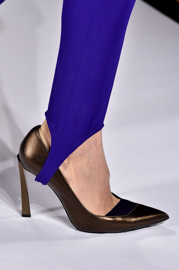 Foto de detalhe do desfile de 2018 da marca francesa Lanvin. Na imagem é possível ver o pé de uma mulher branca usando salto alto dourado e calça legging azul do modelo fusô