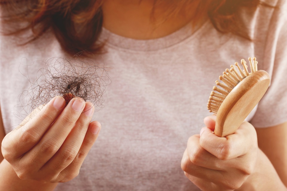 Foto colorida. Mulher chumaço em uma mão e uma escova de cabelo na outra