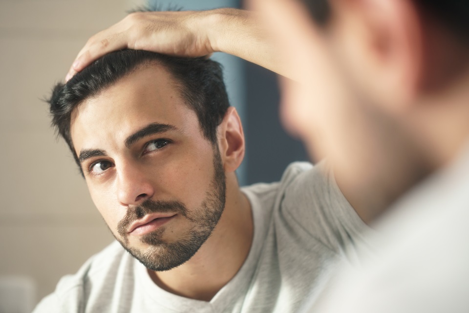 Foto colorida. Homem pegando no cabelo