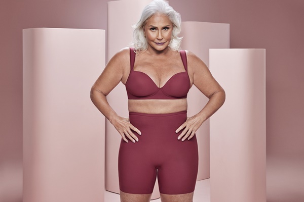 A cantora Fafá de Belém, uma mulher branca e idosa, de cabelos lisos brancos, posando para foto da campanha da marca de lingerie Plié. Ela usa um sutião vinho e um shorts justo na mesma cor