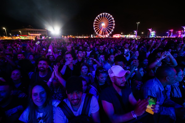 Mutidão de pessoas no festival Rock in Rio, durante um show já à noite. Na foto é possível ver, além da plateia, a roda gigante com luzes coloridas