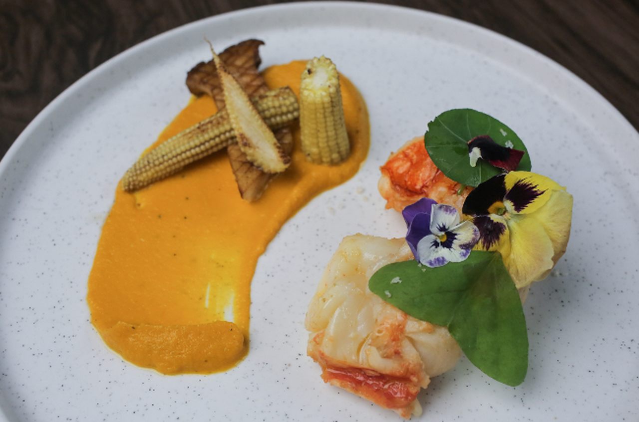 Lagosta confitada na manteiga com creme de cenoura, mini milho, cogumelos porcini e farofa de milho branco