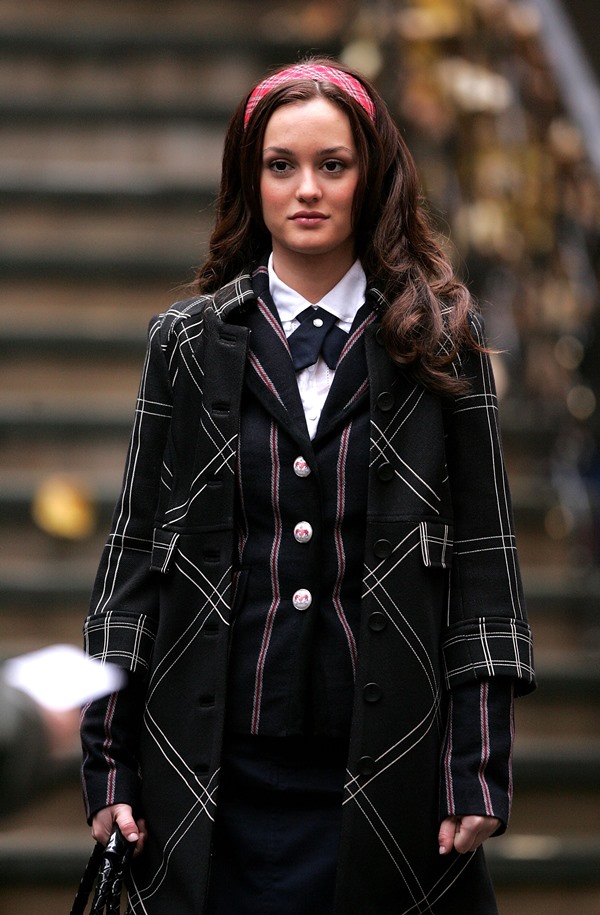 A atriz Leighton Meester nas gravações da série Gossip Girl em 2007. Ela é uma mulher branca e jovem, com cabelo ondulado grande, que veste camisa branca, gravata borboleta, saia e colete, ambos listrados, e um sobretudo preto e branco por cima