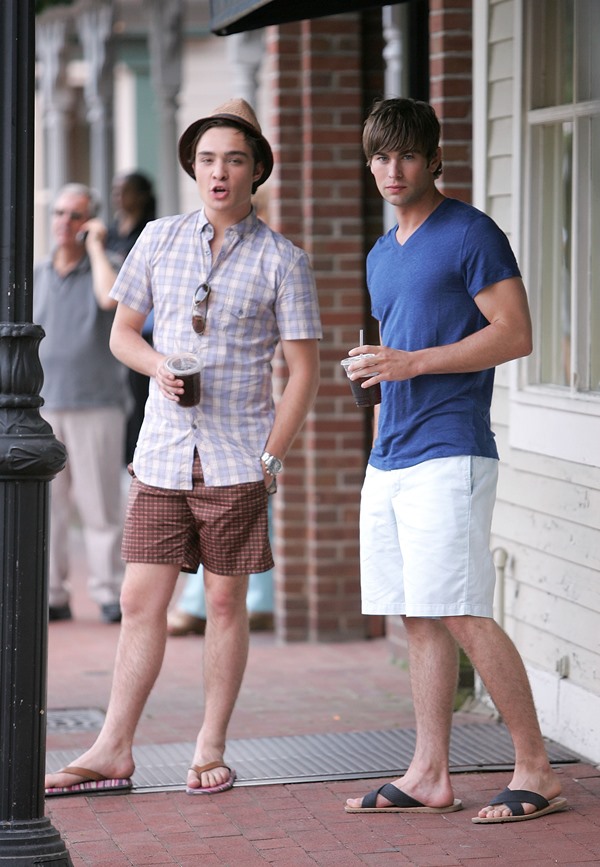 Os atores Ed Westwick e Chace Crawford, ambos atores brancos e jovens, durante as gravações da série Gossip Girl em 2008. Eles usam roupas de verão como bermudas, sandálias, camisas e óculos escuros