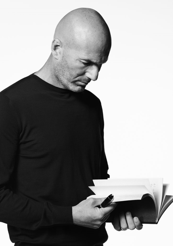 Campanha de divulgação da marca de luxo Montblanc. A foto, feita em preto e branco, mostra o jogador de futebol Zinédine Zidane, um homem branco, de meia idade e careca, com objetos da marca alemã. Ele mostra itens como canetas, pastas e cadernos.