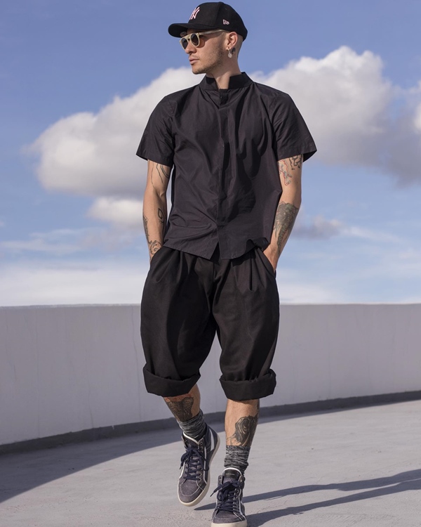 Homem jovem e branco, de cabelo preto e boné, descendo a rampa do Museu da República, em Brasília. Ele usa uma camisa de botão e uma bermuda. As duas peças são pretas.