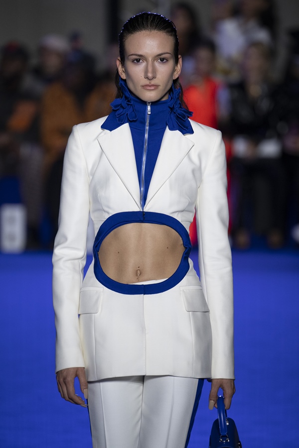 Uma modelo caminha na passarela durante o desfile de moda da marca Off-White, coleção de Primavera/Verão 2023, como parte da Paris Fashion Week em setembro de 2022 em Paris, França. A modelo é uma mulher branca e jovem, de cabelos lisos pretos, e usa um blazer branco com um recorte na barriga e uma calça, também branca