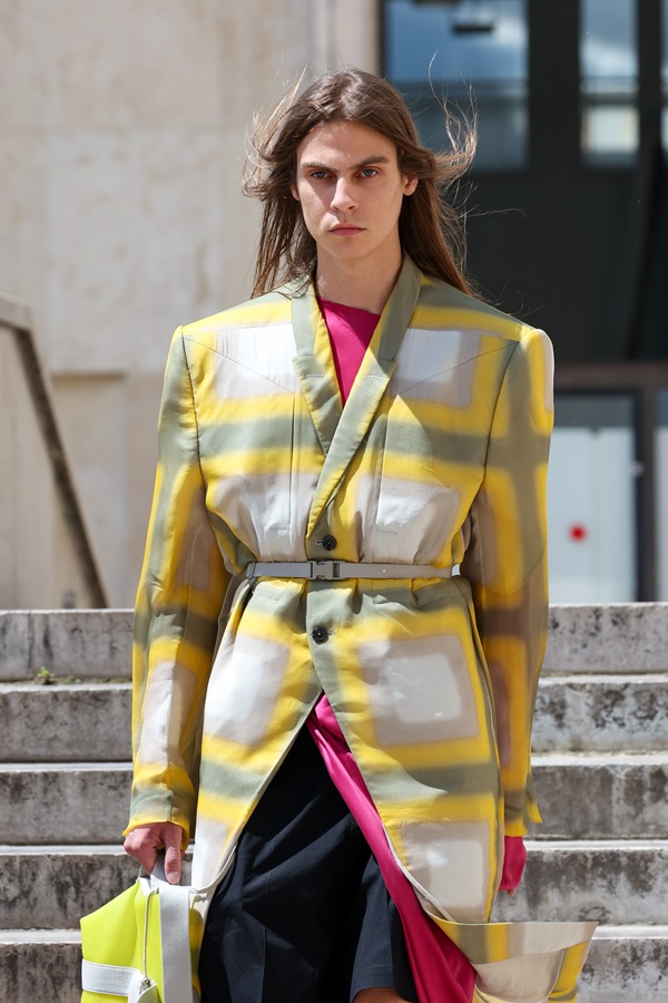 Um modelo caminha na passarela durante o desfile de moda da marca Rick Owens, coleção de Primavera/Verão 2023, como parte da Paris Fashion Week em setembro de 2022 em Paris, França. O modelo é um homem branco, de cabelo grande e liso, que usa um blazer estampado com uma vestido e uma bermuda.