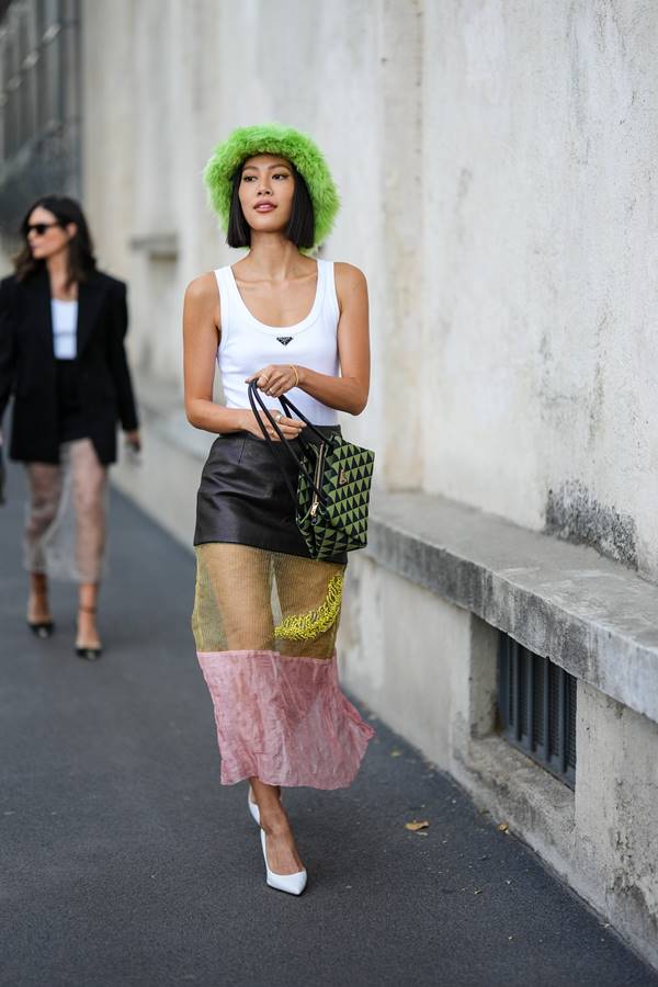 Look com regata branca, saia de couro com barra transparente, e chapéu verde felpudo