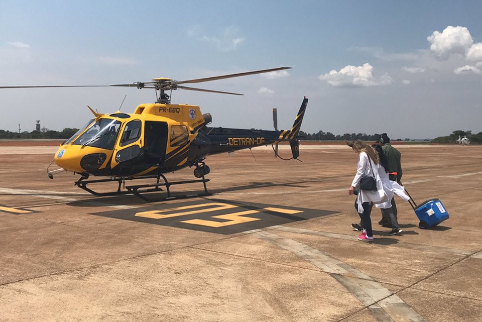 Helicóptero amarelo e preto no chão e pessoas andando com mala