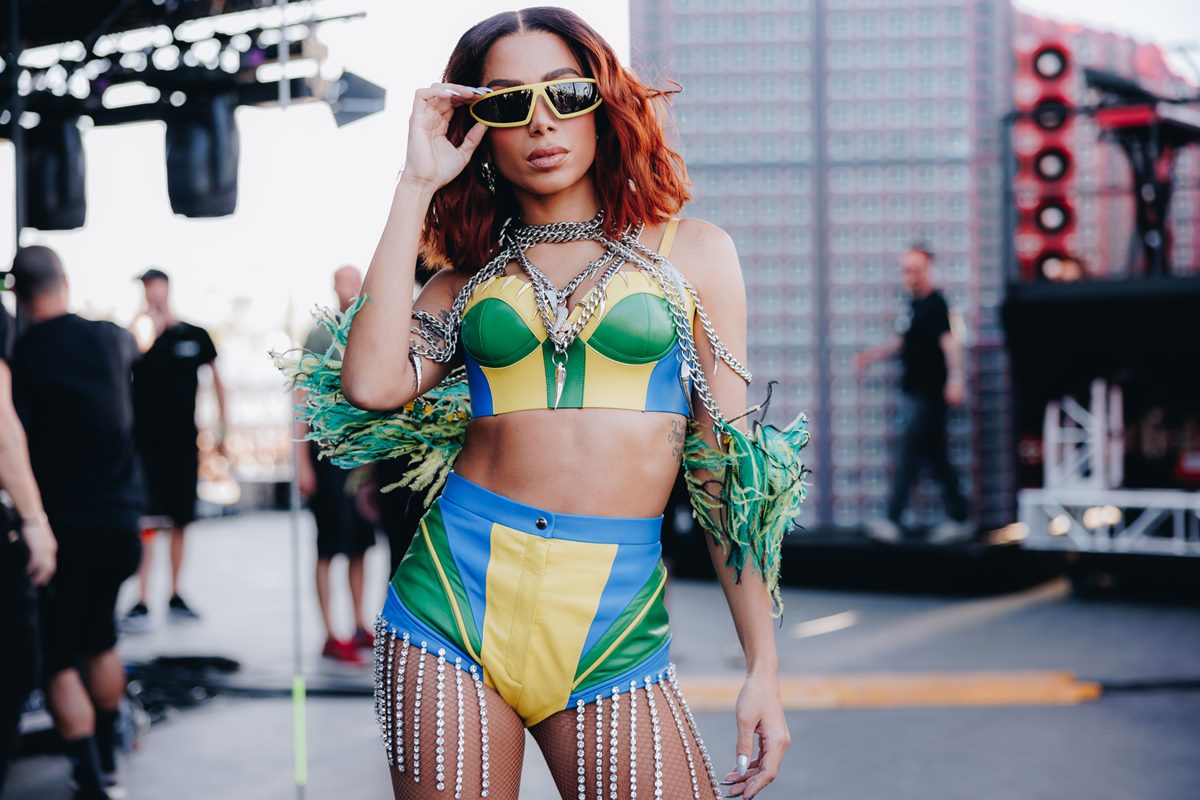 A cantora Anitta no palco do festival Coachella, nos Estados Unidos, em 15 de abril de 2022. Ela usa um top e um short, ambos curtos e de couro, nas cores verde, amarelo e azul, além de um óculos escuro com armação amarela.