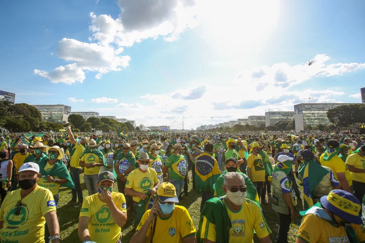 Manifestação pró-Bolsonaro na Esplanada dos Ministérios, em Brasília. Uma multidão de pessoas de diferentes idades usam roupas verde e amarela e seguram a bandeira do Brasil