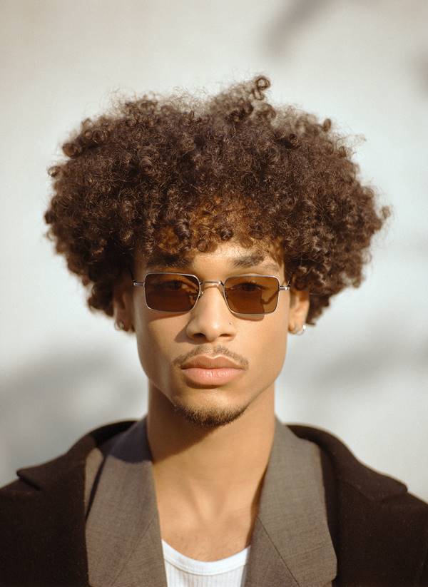 Modelo negro com cabelo cacheado usa óculos com lentes escuras - Metrópoles 