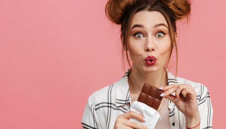 mulher comendo chocolate, fundo rosa , fazendi biquinho - metropoles