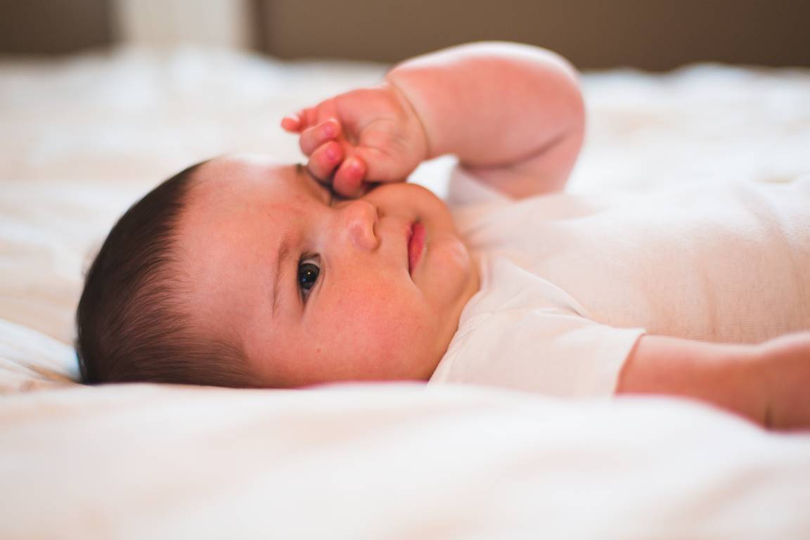 Bebê branco deitado na cama e coçando os olhos