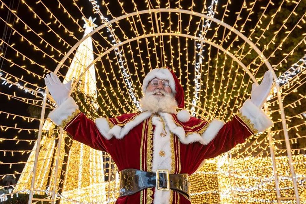 Foto de papai noel com os braços abertos debaixo de muitas luzes