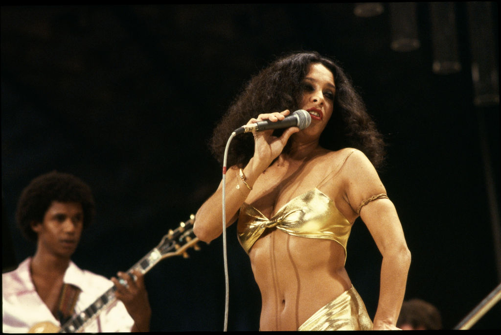 Gal Costa com roupa dourada cantando em cima de um palco - Metrópoles