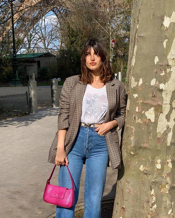 Jeanne Damas encostada em uma árvore usando blazer xadrez, camiseta e calça jeans - Metrópoles 