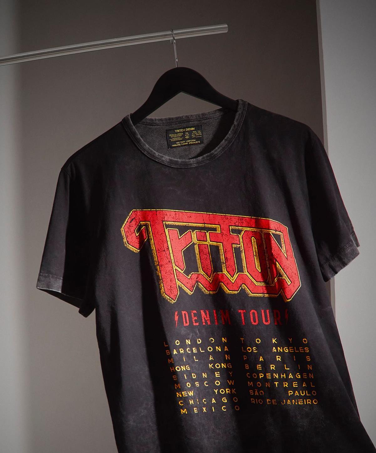 Camiseta preta da marca Triton pendurada em um cabide, também preto. - Metrópoles