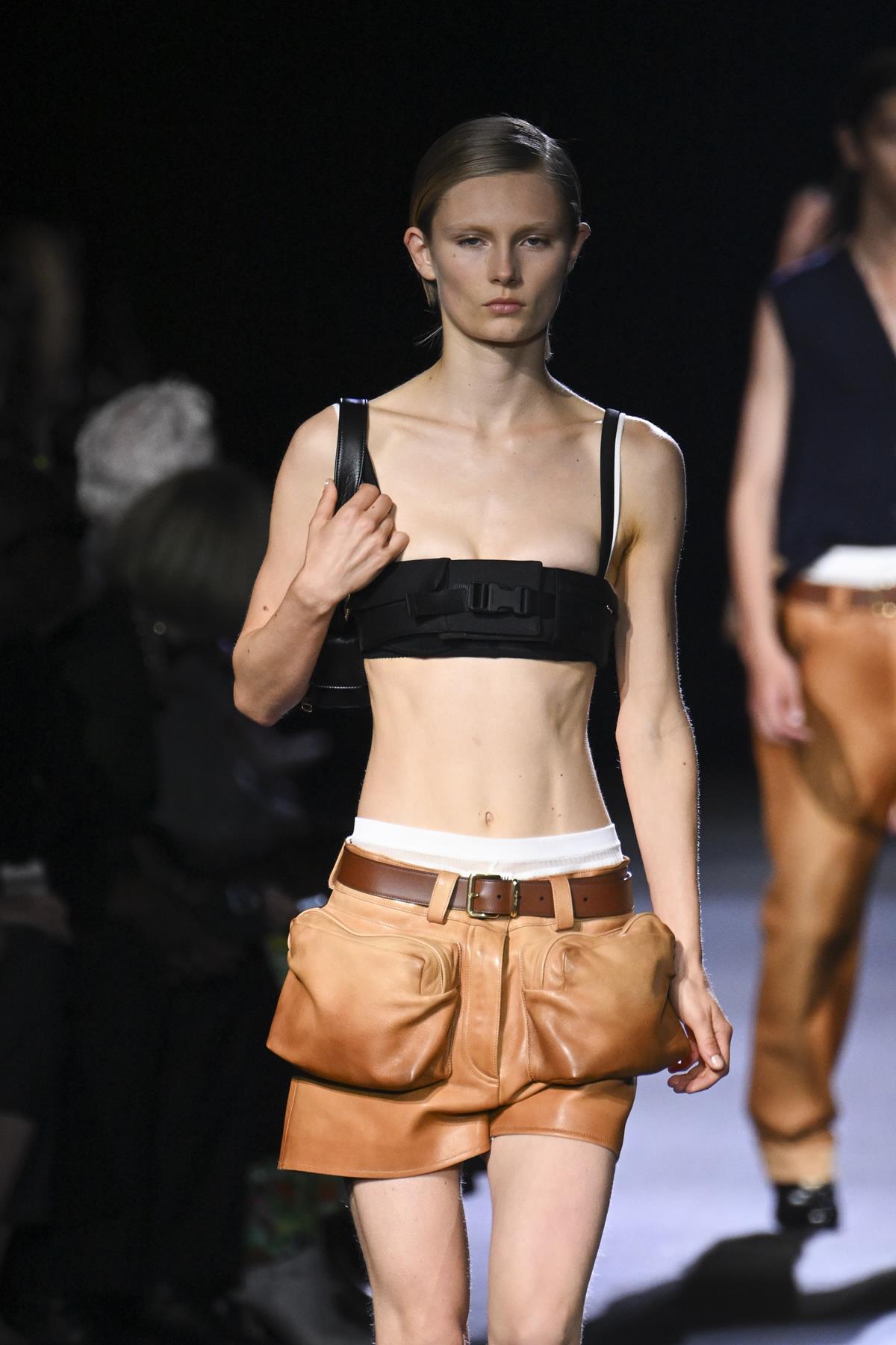 Uma modelo caminha na passarela durante o desfile de moda Miu Miu Ready to Wear Primavera/Verão 2023 como parte da Paris Fashion Week em 4 de outubro de 2022 em Paris, França. Usa um top preto com um shorts marrom caramelo curto. Ela está com a barriga de fora. - Metrópoles