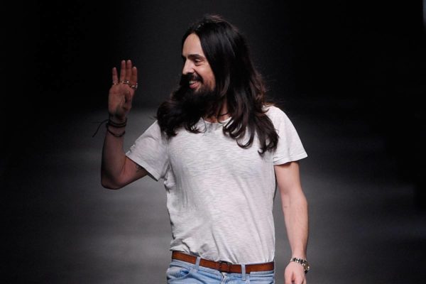 Estlista Alessandro Michele acena para o público após apresentação de desfile. Ele usa camiseta branca, cinto caramelo e calça jeans. Alessandro tem cabelos longos - Metrópoles