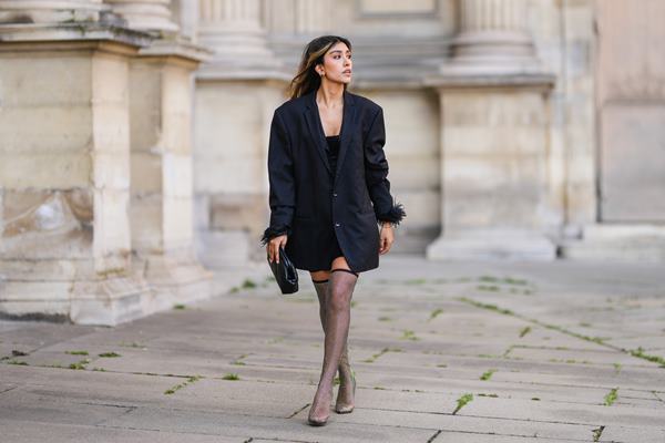 Mulher branca andando na rua. Ela está usando roupas pretas e com botas de strass