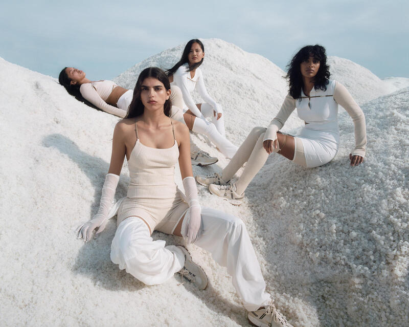 Foto da campanha de divulgação da Nike com a Jacquemus. Na imagem é possível ver quatros modelos jovens usando as roupas, todas brancas, da coleção. Elas estão enconstadas em pedras brancas. O cenário parece de um filme de ficção científico. - Metrópoles