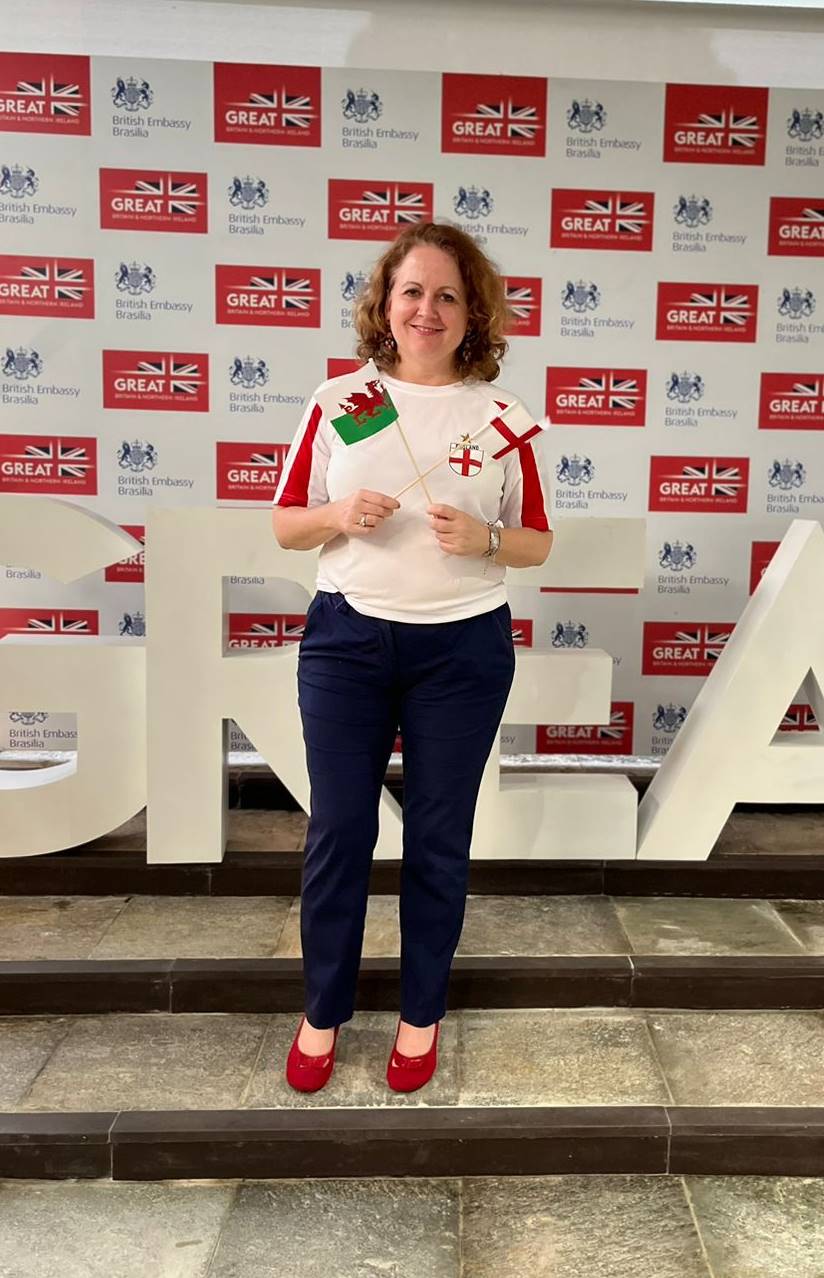 Mulher branca vestindo camisa da seleção da Inglaterra segurando uma bandeira da Inglaterra e do País de Gales