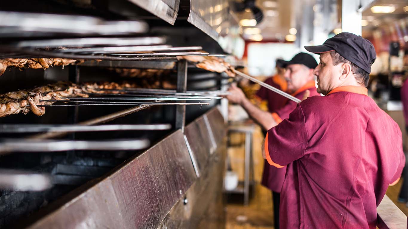 Churrasqueiro prepara frango assado na churrasqueira do restaurante O Brazeiro, em SP