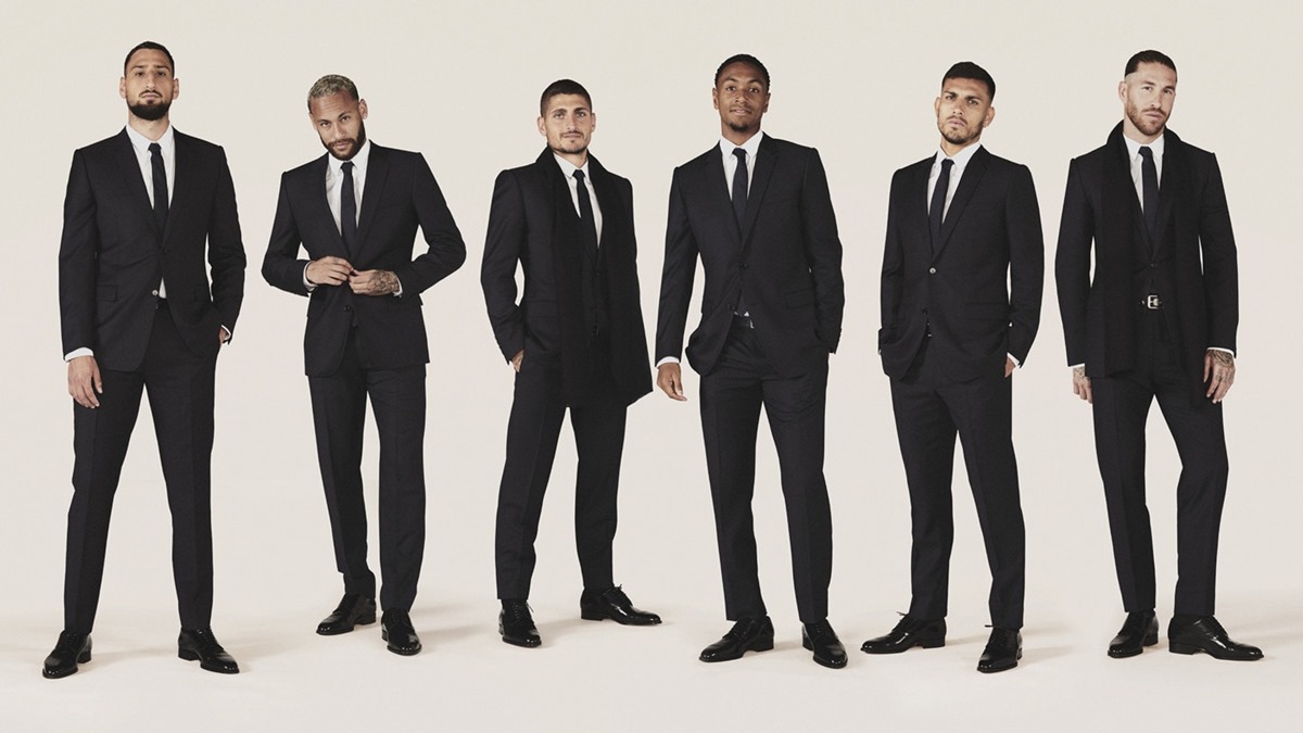 Jogadores do time Paris Saint-Germain em foto publicitária da marca Dior. A imagem foi registrada em um estúdio, em um fundo branco, e os jogadores usam ternos e gravatas. - Metrópoles