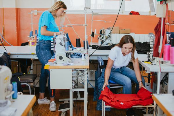 Na imagem com cor, duas mulheres em fábrica de vestuário - Metrópoles