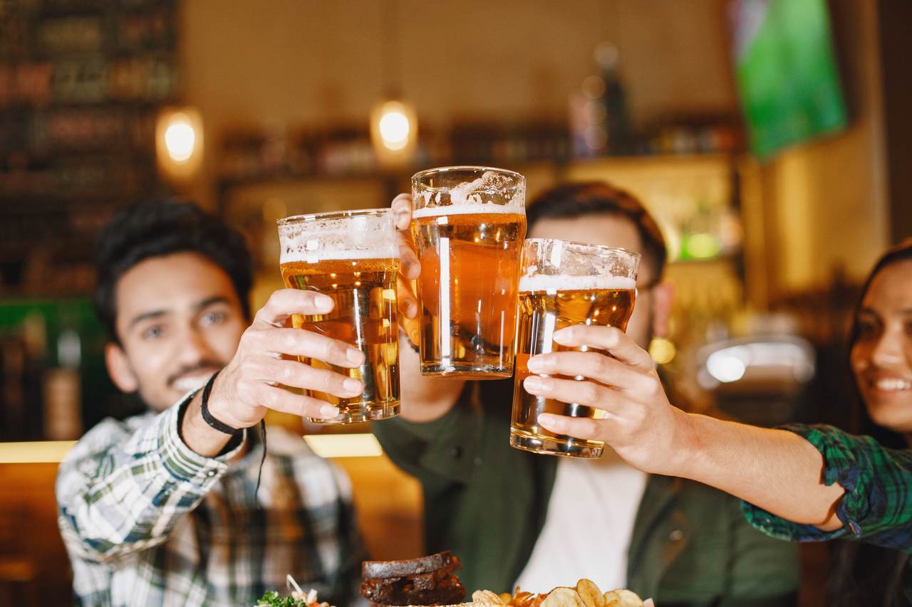 Na foto, três pessoas brindam com caneca de chope - Metrópoles