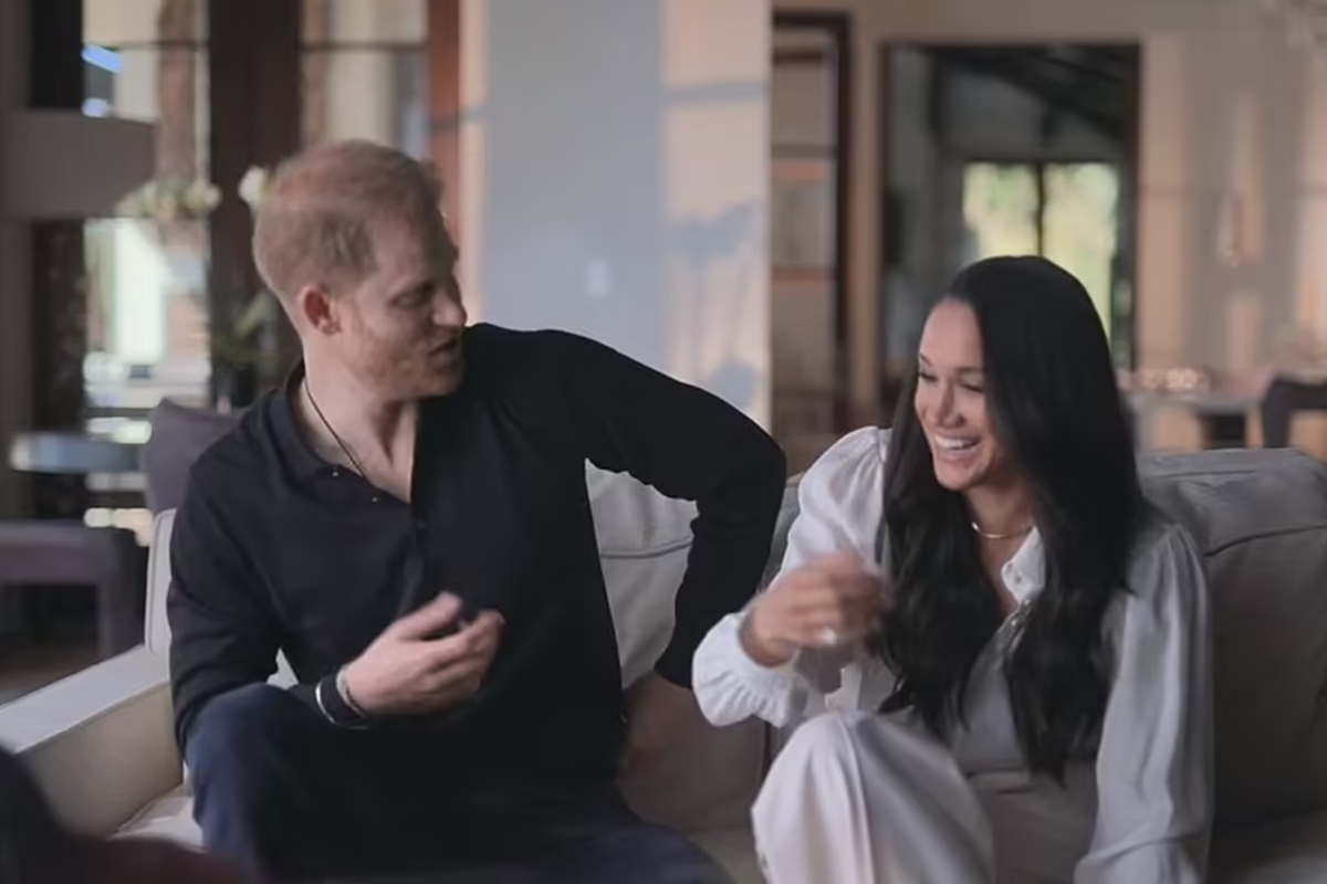 Foto colorida de homem branco, ruivo e com roupas pretas sentado ao lado de mulher, parda e com roupas brancas. Ela está sorrindo - Metrópoles